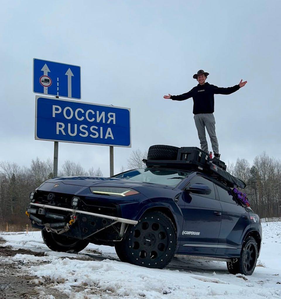 «Кругосветный» блогер Camperghini пересёк белорусско–российскую границу.    8 марта американец выложил в своём аккаунте очередное фото с подписью: «Welcome to Russia!».  Коннор отправился в кругосветное путешествие в 2023–м, продав дом и купив Lamborghini Urus с пробегом в 30 тыс. км, сделав из него кемпер.  Camperghini ночует и готовит в машине, в шутку называя себя бомжом. РФ станет 32-й страной его маршрута.  В комментариях к записям больше всего замечаний об опасностях путешествия по нашей стране и сомнений в том, что её негде будет заправить  «Урус» кушает 22 л. хорошего бензина на сотню км  и починить.  Lamborghini Urus  VW  построен на одной платформе с Audi Q7 и Porsche Cayenne. А именно на Audi Q7 наша команда из двух человек проехала из Москвы до Владивостока и обратно. Машина у Коннора не новая, но вполне свежая  в кругосветке он накатал ещё 55 тыс. км . На пробег вокруг глобуса хватит.  Можем успокоить: на большей части РФ ему угрожают только ДТП, подставы и жулики  опасаемся за запаску на крыше – колесо «Ламбы» может стоить дороже нового бюджетного авто .  Откровенно рискованные только «тёмные территории» – 1,5 тыс. км между Читой и Благовещенском. С приличным бензином там тоже проблемы. Но и там мы встречали таких «отмороженных» путешественников.  Сейчас блогер нарезает километры по российским дорогам.  После России собирается ещё лет пять кататься по Азии, Африке и Южной Америке. Пожелаем удачи.