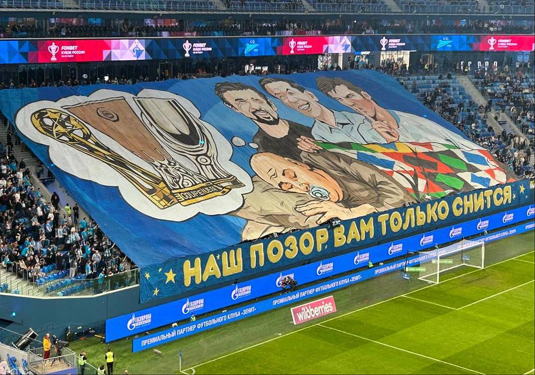 Фанаты Зенита высмеяли кричалку Зенит позор российского футбола вывесив баннер перед матчем с Динамо в Кубке России На полотне изображён взрослый лысый мужчина с соской во рту который укрыт одеялом в цветах клубов РПЛ от красно белых до чёрно зеленых Мужчине над которым стоят Семак Аршавин и Зырянов снятся Кубок УЕФА Суперкубок УЕФА и трофей РПЛ а под баннером написано Наш позор вам только снится Зенит единственный клуб России у которого есть все эти трофеи