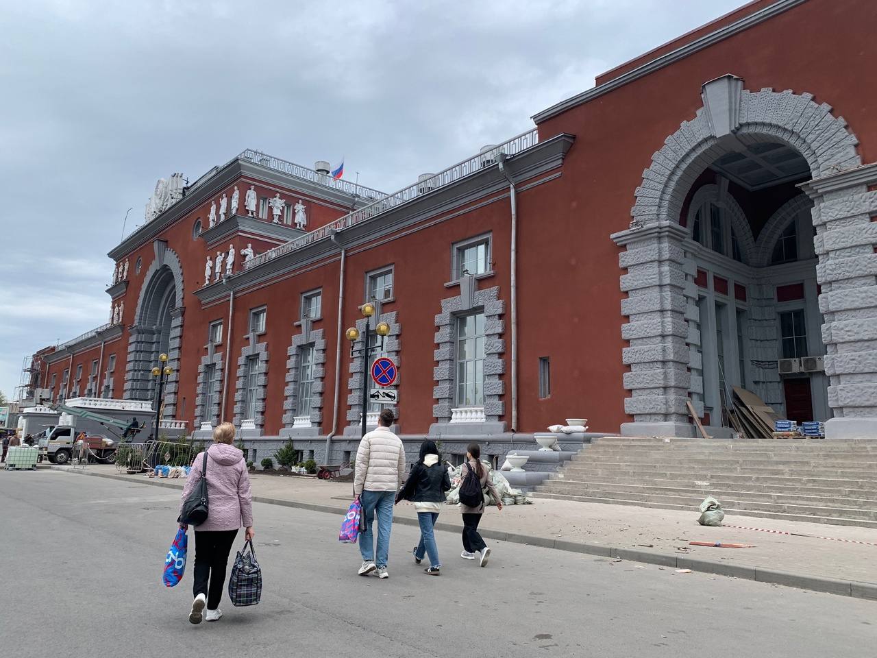 В Курске закончилась реконструкция фасада железнодорожного вокзала: зданию вернули историческое цветовое решение . Цвета до и после сравнило на фотографиях издание «Друг для друга». Теперь красная терракотовая штукатурка сочетается с серыми карнизами, рустами, обрамлениями арок, окон и цокольного этажа. Раньше элементы были более светлыми, почти белыми. Само здание, построенное в 1952 году архитектором Игорем Явейном взамен пострадавшего от авианалетов вокзала - это памятник военной эпохе. Арки и полусводы - это не только образ огненной дуги, это одновременно триумфальная арка, ворота в город и дань традиционной русской архитектуре. Автор проектов более ста вокзалов, Явейн был поклонником конструктивизма, но в эпоху запрета на него и торжества сталинской неоклассики архитектор, фактически, сформировал свой стиль. Здание Курского вокзала стало первым в этом ряду. Оно впитало в себя планировочные особенности того же конструктивизма, но подобрало ещё и черты сталинского ампира, одновременно став отсылкой к русской архитектурной традиции. Специалисты считают, что сочетание терракотового цвета, темно-красная терразитовая штукатурка с серыми частями - это именно один из признаков национальной архитектуры. У курских краеведов, впрочем, другая версия. Они убеждены, что Игорь Явейн планировал сделать вокзал бирюзовым, но «цвет запекшейся крови» на здании-памятнике придумал выбрать лично товарищ Сталин. На этом в частности настаивает Александр Манжосов. На фото цвета до и после