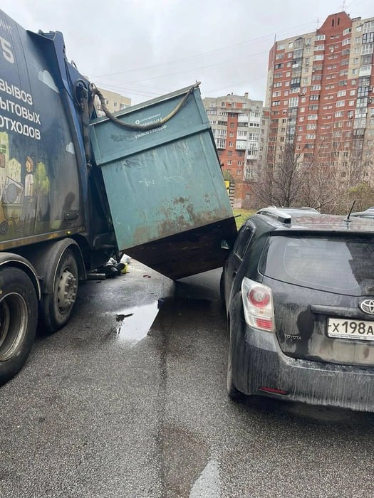 Неприятная картина ожидала утром владельца автомобиля, припаркованного у мусорной площадки в Приморском районе. Транспорт оказался подмят под весом слетевшего с мусоровоза металлического контейнера, но виноват в этом может быть вовсе не его водитель, а недобросовестные горожане.  Инцидент произошел около 10 часов утра водитель мусоровоза сам обратился в полицию. Судя по опубликованным в сети кадрам, автомобиль стоял у подъезда к контейнерной площадке. Удар пришелся на угол капота с водительской стороны, у машины как минимум помята верхняя крышка и разбита фара. А мусоровоз числится за городской компанией ООО «Сити-Клининг».   «Такая коллизия произошла из-за того, что был нарушен порядок накопления: в данный контейнер незаконно были сгружены строительные отходы, в результате чего произошёл перегруз, наклонило бак. И вот так он неаккуратно повредил машину. …Вот к чему приводит складирование строительных отходов жителями. А водителю этому можно посочувствовать из-за испорченного настроения, потраченных времени и нервов», — сказали в пресс-службе АО «Невский экологический оператор».  Там отметили, что ситуация спорная и определить, кто именно должен возместить автомобилисту ущерб, предстоит еще разобраться. Ситуацию обсудили и в группе «Приморский район», пользователи уверены, что инцидент станет уроком как для конкретного автомобилиста, так и для всех водителей, которые преграждают проезд спецтранспорту.     АО «Невский экологический оператор»