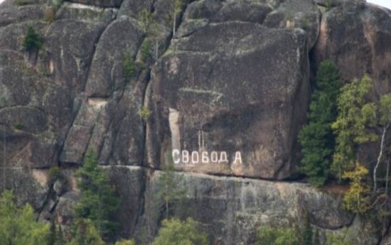 Власти Красноярска заретушировали слово "Свобода" на фото скалы из нацпарка "Столбы".  Слово, написанное белой краской, появилось на откосе одной из скал в конце 19-го века. Изначально его нанес политический ссыльный по фамилии Островский вместе.   Позже его не раз стирала полиция, но его постоянно наносили снова. Надпись и сейчас расположена на горе.  В администрации ретушь "Свободы" объяснили плохим качеством фото. Якобы при увеличении объекта надпись стала "более пиксельной" и ее пришлось убрать.    "Красноярские столбы" считаются одним из старейших охраняемых природных объектов в России. Он получил свое название из-за характерной формы скал. Надпись "Свобода" находится на Втором столбе.    В 19-том веке Столбы стали пристанищем активистов, недовольных властью. Их движение получило название "столбизм".