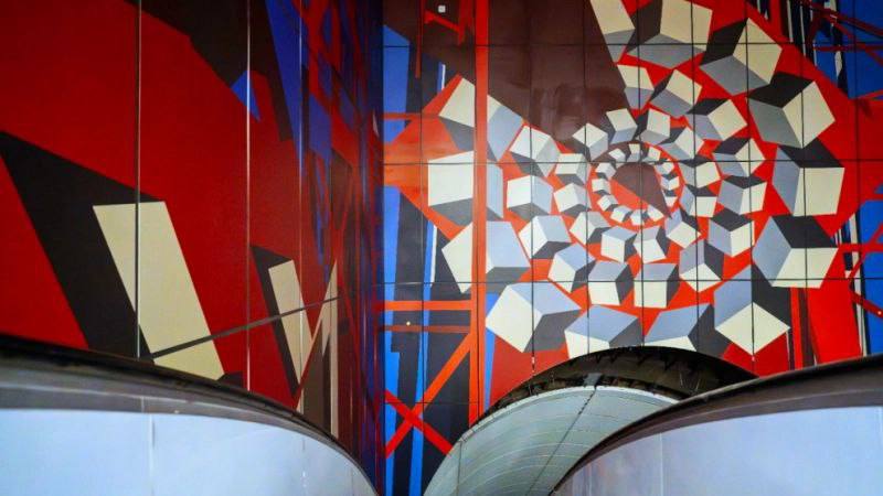 В Петербурге звершен монтаж панно в вестибюле станции новой линии Путиловская Петербургские метростроители завершили монтаж масштабного панно в вестибюле станции новой Красносельско Калининской линии Путиловская Оно выполнено из сотовых алюминиевых панелей с печатью Художественное решение основано на истории Путиловского завода и абстрактно отражает машиностроительное чугунное и художественно литейное производства Ширина расположенного над эскалаторами панно варьируется от 8 до 15 с небольшим метров Сейчас на станции Путиловская завершается облицовка фасада одноэтажного вестибюля и его внутреннее обустройство В наклонном ходе смонтированы водоотводящие зонты метростроители установили четыре эскалатора Размещаются необходимые инженерные сети и системы На финальной стадии находится отделка кассового зала природным камнем уже облицованы стены и полы