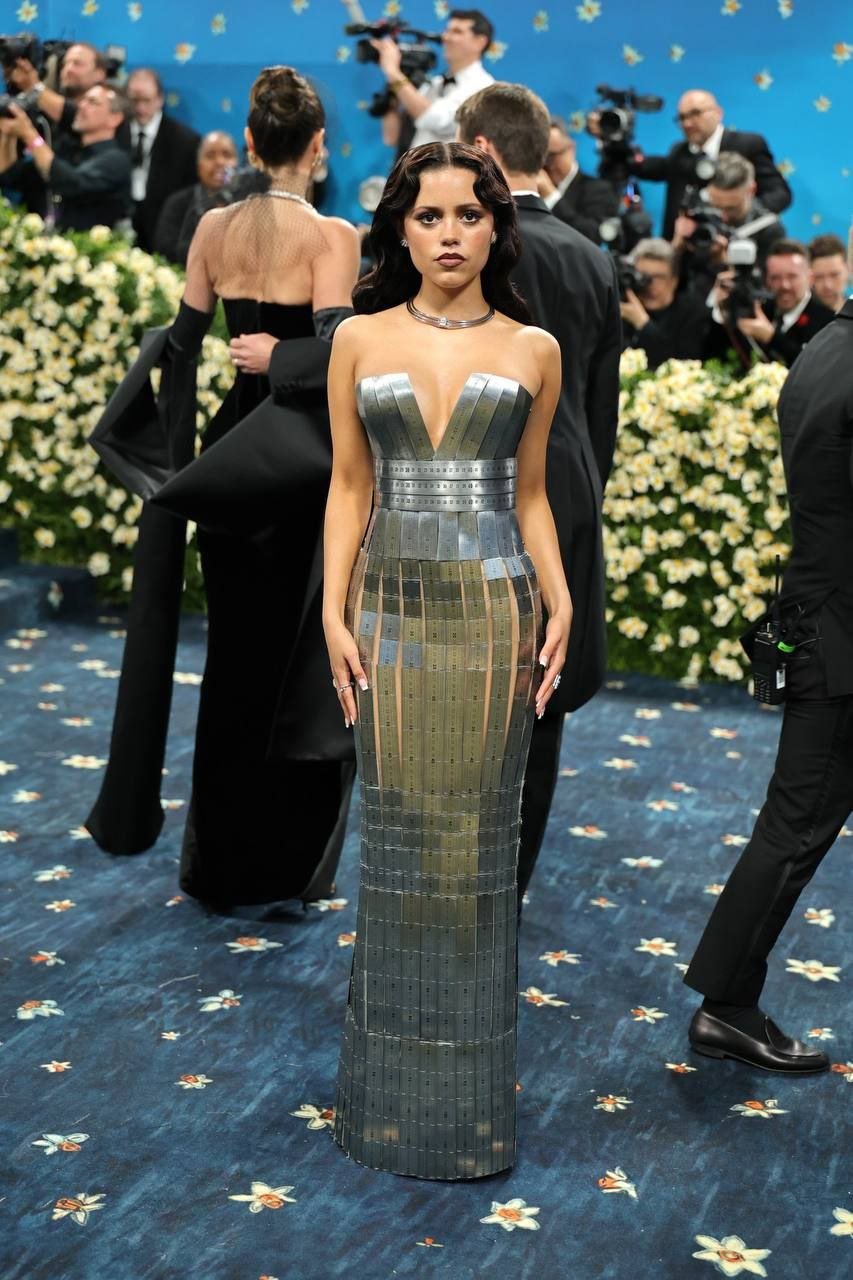 Ну что, Met Gala отгремел. В этом году тема бала "Сшито для вас". Выставку в музее посвятили моде темнокожих дэнди начала XX века. Так что большинство селеб обратилаось к гарлемским архивам: были белые смокинги, джазовые костюмы 40-х, очень много полоски. Разумеется, много отсылок к знаменитой "Чёрной жемчужине" - танцовщице Жозефине Бейкер. Выбрала наряды, которые запали в сердце и попали в тему бала. Дженна Ортега скорее бонусом, мне понравилось это платье словно из измерительных линеек. Кринжа было тоже достаточно, но такого кислого, что даже разбирать неинтересно. Местами творился полный сюр: на улице толпились протестующие Палестина/Израиль , а на ковровой дорожке перед ними Анна Винтур пританцовывала под выступление хора. Рианна по традиции явилась последней и выбрала Met Gala для объявления о третьей беременности. Раньше было прикольно, но с каждым годом выходка теряет своё очарование. Ну и на мой плебейский вкус костюм Рианны вышел средненький. Помятуя о прошлых выходах, я знаю, что Рири могла лучше. А ещё остро не хватало главного темнокожего дэнди Нью-Йорка Андрэ Леона Телли. Вот бы кто раздал стиля этому вечеру. Ещё один год, когда мне кажется, что Met Gala теряет свой глянцевый лоск. Как будто 2018-й стал последним хорошим годом для бала. Как мы тогда верещали с шикарных костюмов! А кринжа была такая сочная, что даже было хорошо. Сейчас я быстро пролистываю фотки, вздыхаю над худшими костюмами, выбираю те, которые "вроде ничего" и на этом успокаиваюсь. Надеюсь, кто-то однажды придёт и раскачает эту лодку сонных сытых селеб, прежде чем Met Gala пойдёт ко дну окончательно.