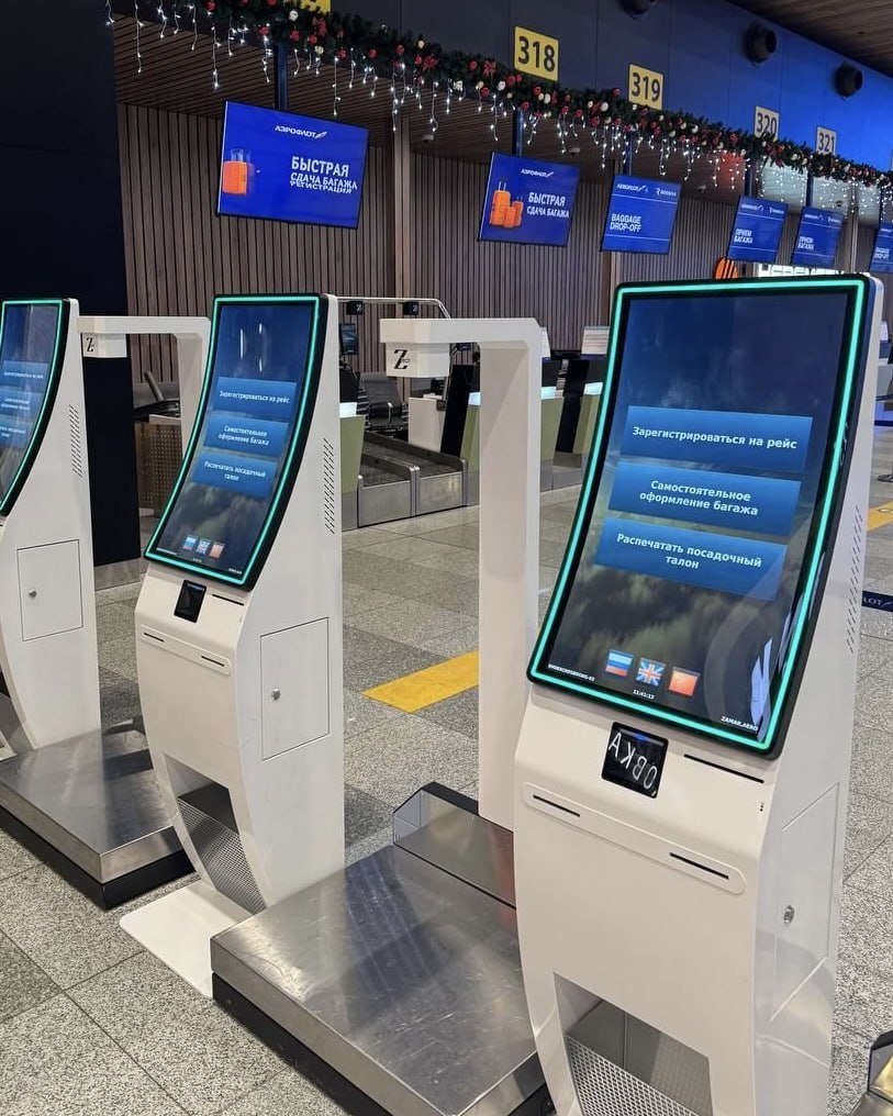 В терминале Шереметьево B запустили киоски саморегистрации багажа В терминале B аэропорта Шереметьево заработали 10 новых киосков для самостоятельной регистрации на рейс Воспользоваться ими могут пассажиры Аэрофлота и России вылетающие внутренними рейсами Их главное преимущество возможность самостоятельно не только зарегистрироваться на рейс это и в мобильном приложении или на сайте можно сделать но и оформить багаж Рядом с каждым киоском находятся весы а также сканер определяющий габариты чемодана или сумки Если всё проходит по весу и размерам то киоск печатает багажную бирку которую нужно самостоятельно наклеить и отнести чемоданы на ленту после чего они уедут на сортировку С логической точки зрения процесс регистрации и оформления багажа ничем не отличается от регистрации на стойке но возле них нет очередей Во всяком случае пока большинство пассажиров ещё не знает о новых киосках кроме того судя по предыдущему опыту аэропорта Шереметьево подход женщину вынули автомат засунули на этой планете импонирует не всем особенно старшему поколению Однако это неизбежность доля тех кто родился с дисплеем в руках среди пассажиров растёт а тех кто этих ваших конпуктеров боится сокращается Так что в перспективе авиакомпания намерена увеличивать количество стоек самостоятельной регистрации в базовом аэропорту Для обычной регистрации держать живого человека и правда не стоит нужны квалифицированные специалисты для сложных ситуаций Раньше киоски саморегистрации уже были установлены в нескольких аэропортах страны однако в 2022 году прекратили работу в связи с переходом всех российских авиакомпаний на отечественное программное обеспечение А такие киоски поддерживались только зарубежным софтом В начале 2024 го поддержка киосков появилась в ORS DCS которой пользуются только S7 и Азимут весной 2025 года её завезли и в Астру на которой в России работают все остальные авиакомпании Тогда же подняли на российском софте 3 старых киоска интегрированных со стойками регистрации Теперь же в дополнение к ним установили 10 более современных отдельно стоящих аппарата www frequentflyers ru 2025 12 10 svo kiosk frequentflyers