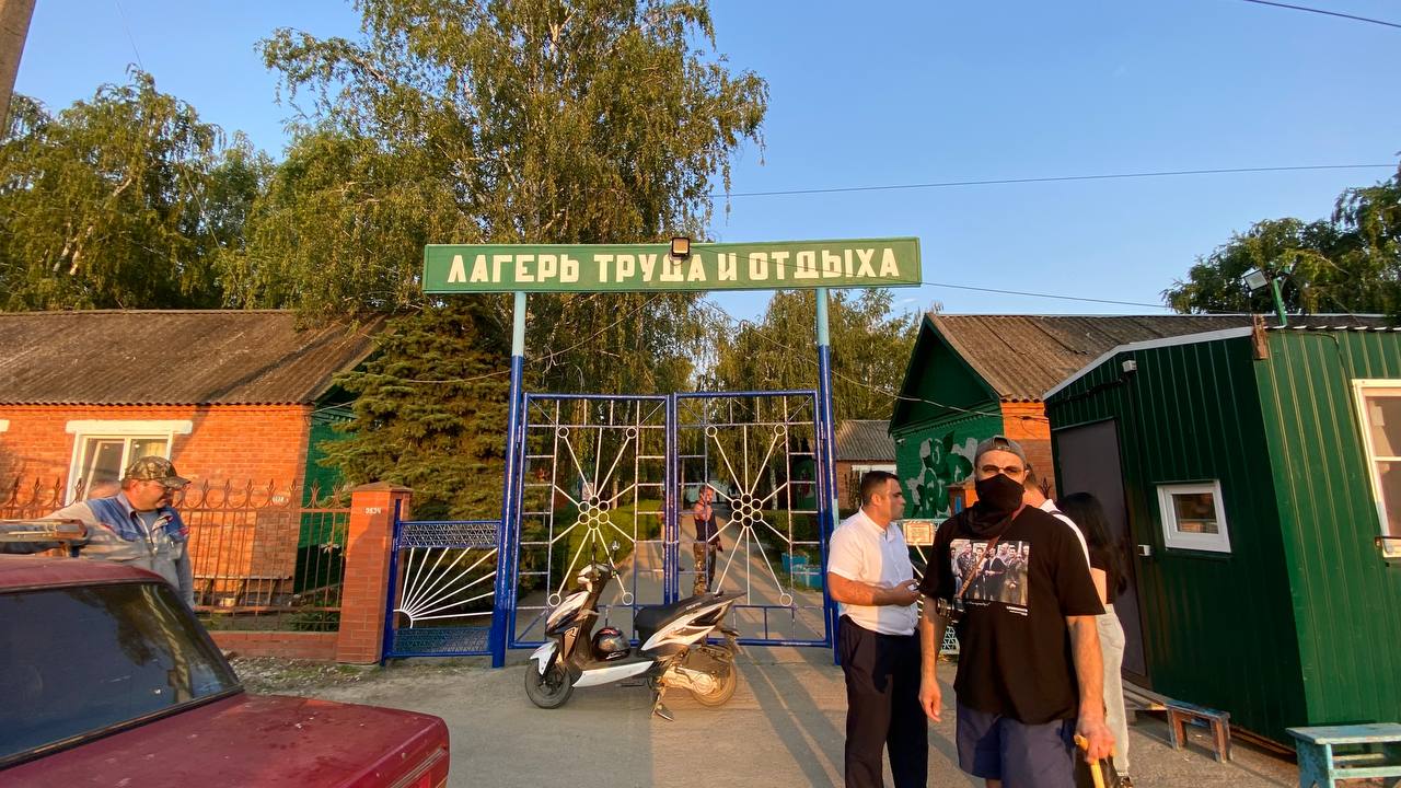 Под Славянском-на-Кубани в небольшом поселке волонтеры движения «Альтернатива» и журналисты нашли большой трудовой лагерь. Место это можно легко спутать с детским лагерем, но вместо детей там десятки пьяных людей, которых свезли из разных регионов страны. Одни объявлены в розыск родственниками, другие содержатся там без паспортов. Работают эти люди в яблочных садах одного из крупнейших производителей фруктов. Рабочие месяцами живут в кирпичных одноэтажных постройках по 8-10 человек. Практический каждый, с кем удалось поговорить, жалуются на отсутствие зарплат и систематическое спаивание для подавления воли. Вся эта история очень сильно напоминает рабство, а сам лагерь — огромный «работный дом». Рассказываем в нашем материале, как в маленьком кубанском поселке нашелся большой «трудовой лагерь».