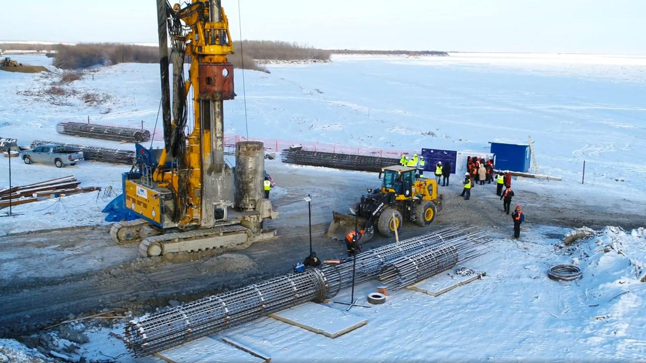 20 свай первой опоры Ленского моста забетонировано в Якутске  Первой будет возведена опора №6, всего под нее установят 32 сваи. Сейчас в работе находится 21-я.  Согласно проекту, будет построено четыре опоры на левом берегу, три - в русловой части Лены и 19 - на правом берегу. Под них предстоит устроить 920 свай, на это уйдет около 48 тысяч кубометров бетона.   Бетонировать сваи продолжат до прихода сильных морозов. Когда потеплеет, строители начнут устраивать конструктивы опор  ростверки, тела  и шпунтовые ограждения котлованов.  «На правом берегу завершена сборка бетонного завода в зимнем исполнении, выполнены пусконаладочные работы для обеспечения выпуска необходимой смеси. Готов навивочный станок для создания арматурных каркасов свай», - сообщили в группе «ВИС».   Фото: группа «ВИС»