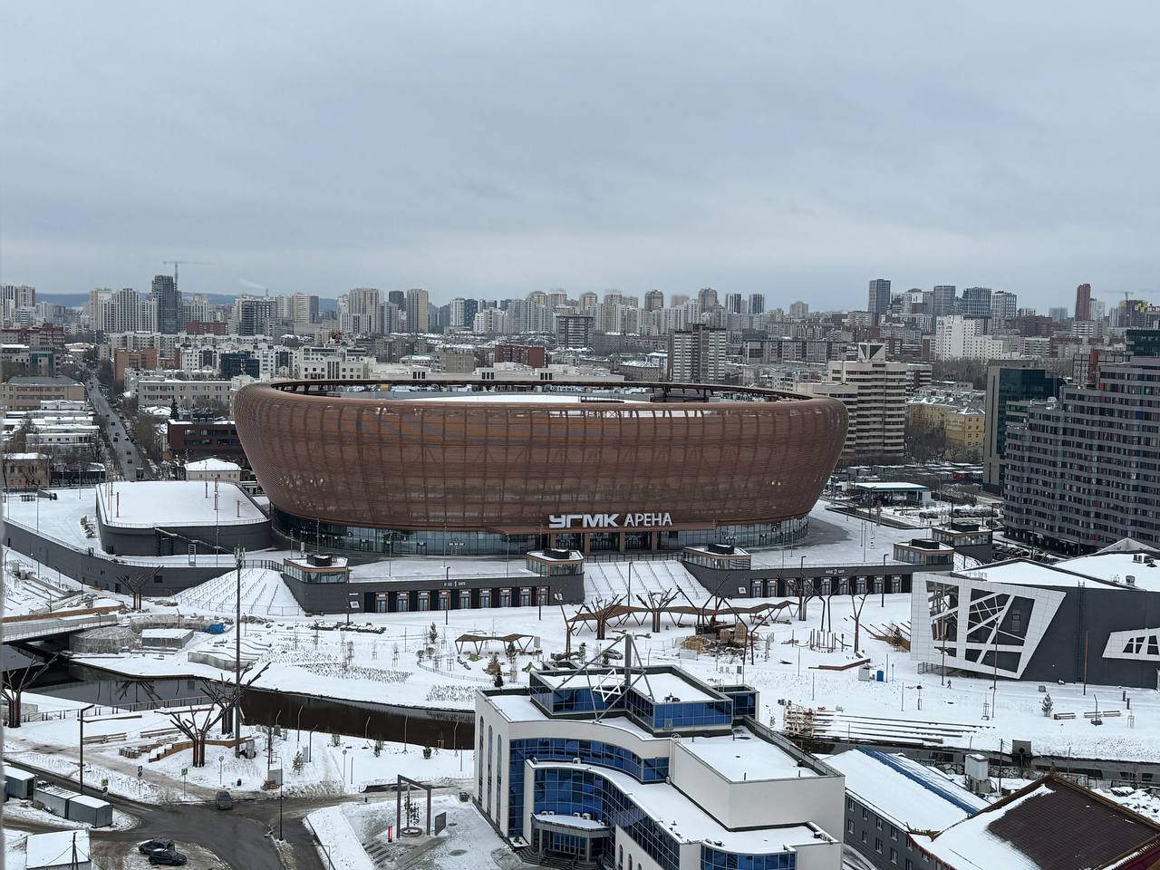 Официально и почти в срок в центре Екатеринбурга закончили строительство новой ледовой арены.   «УГМК Арена» построили на месте снесенной телебашни. Финала стройки этого объекта ждали многие. Во-первых, первые матчи уже должны начаться в конце февраля. Во-вторых, организаторы масштабных ивентов ждали «зал» в центре Екатеринбурга, где с парковкой будет все хорошо, со звуком и с посадкой. Новая арена рассчитана на 15 тысяч зрителей, если мы говорим про концерты  там полностью можно будет закрыть лед и переоборудовать площадку под любой ивент . Спортивные мероприятия будут вмещать до 12 тысяч зрителей. В 2020 году стоимость объекта оценивали в 23 млрд рублей, на сегодняшний день цифры закрыты.    УГМК к запуску арены подтянули свои мощности и по гастрономии. Их фабрика будет обеспечивать кейтеринг любым форматам мероприятий. Кроме того, на арене построили порядка 30 корнеров с разными направлениями по кухне и ресторан. Просчитали и детскую историю. Плюсом, будут работать мобильные пункты на время матчей. Команда управленцев арены имеет опыт работы на Чемпионате Мира по футболу.    Правда благоустройство вокруг арены получилось абсолютно "голым". При запуске стройки была полностью уничтожена зеленая зона - вырублены все деревья на берегу Исети. Компенсации озеленения на территории, прилегающей к арене, нет. Хотя дизайнеры решили выстроить на площадках вдоль реки и арены искусственные деревянные деревья-светильники.     Миллионеров