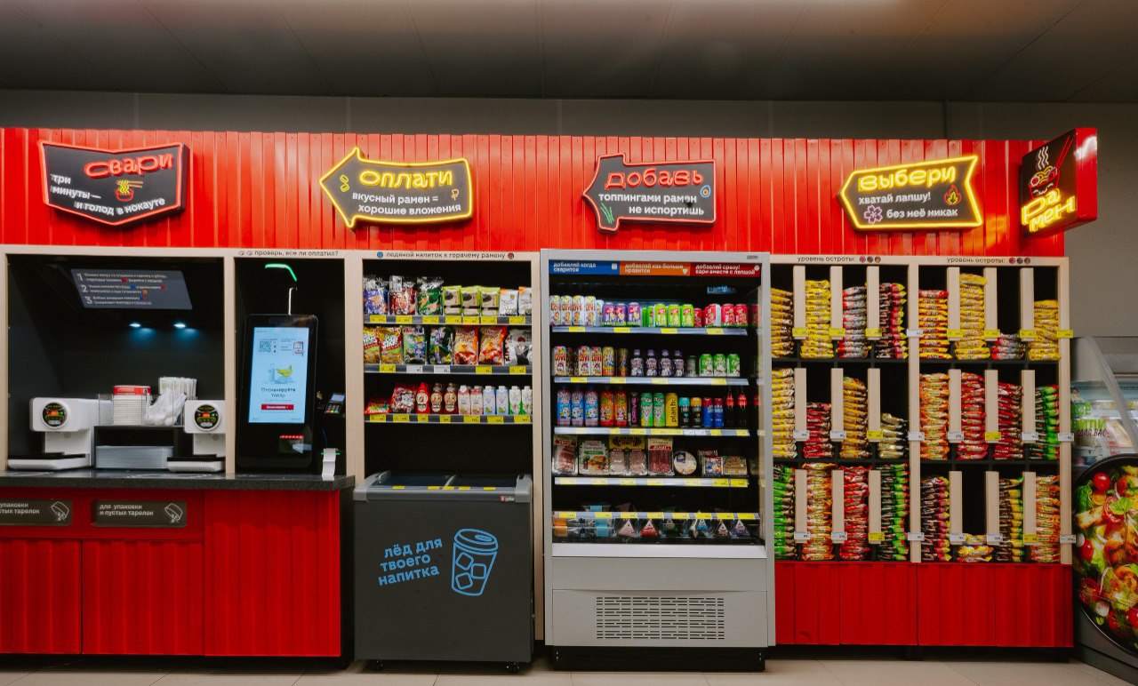 Магнит продолжает развивать сервисы готовой еды в своем ключевом формате магазинах у дома В январе ритейлер открыл сразу 24 новые раменные в магазинах у дома в 11 городах Раменные от Магнита работают по принципу самообслуживания различные виды лапши и топпингов в индивидуальных упаковках помещены на специальных автоматизированных витринах покупатель выбирает ингредиенты оплачивает заказ и готовит блюдо в раменоварке В списке городов где в магазинах у дома открылись раменные Москва Санкт Петербург Краснодар Екатеринбург Казань Новосибирск Воронеж Пермь Самара Саранск и др Для открытия рамённых выбираются локации с активным трафиком особенно молодежным вблизи вузов В раменных от Магнита представлено до 15 видов топпингов которые покупатель может добавлять в блюдо по своему вкусу говядина филе индейки грибы морепродукты яйца и др В компании рассказали что в ближайшее время предложат потребителям несколько новых вкусов в числе которых имбирный язык говядина спайси курица в соусе лемонграсс лайм утка в пяти специях и др Напомним что Магнит открыл первую раменную в магазине у дома в августе 2025 года в Москве До конца года компания открыла еще несколько таких точек в Москве и Петербурге На конец января 2026 г в магазинах Магнит у дома работают более 30 раменных самообслуживания PRORETAILCOMMUNITY