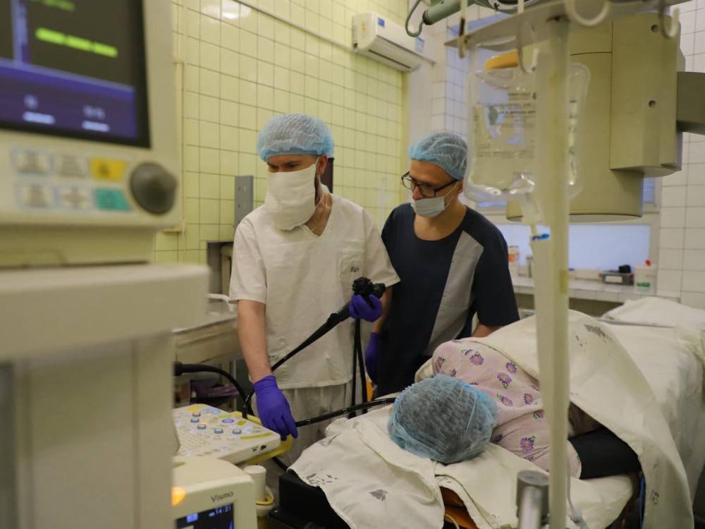 Архангельские врачи помогли 101 летней пациентке избавиться от камня в желчном пузыре Забыв про свой почетный возраст женщина не побоялась лечь на операционный стол а медики провели вмешательство крайне аккуратно с помощью эндоскопа Несмотря тяжелые сопутствующие заболевания специалисты смогли помочь женщине выбрав максимально щадящую тактику лечения У пациентки обнаружили крупный камень в желчном протоке и серьезные осложнения С учетом всех рисков вмешательство провели эндоскопически аккуратно и бережно операция завершилась успешно Губернатор Архангельской области Александр Цыбульский поблагодарил медиков за профессионализм Подобные результаты это всегда сочетание опыта врачей и современных технологий В Первой городской клинической больнице имени Волосевич работает центр гепатопанкреатобилиарной хирургии и интервенционной эндоскопии Здесь ежегодно проводят тысячи исследований и высокотехнологичных операций что позволяет выявлять заболевания в том числе онкологические на самых ранних стадиях Центр развивается благодаря активности и постоянному профессиональному росту коллектива Команда больницы регулярно проходит стажировки в ведущих российских клиниках осваивает новые технологии и внедряет методы которые еще недавно были доступны только в федеральных центрах Например врач эндоскопист Сергей Поздеев провел сотни эндоскопических вмешательств в том числе у пациентов пожилого возраста с тяжелыми сопутствующими заболеваниями Фото пресс службы областного Минздрава