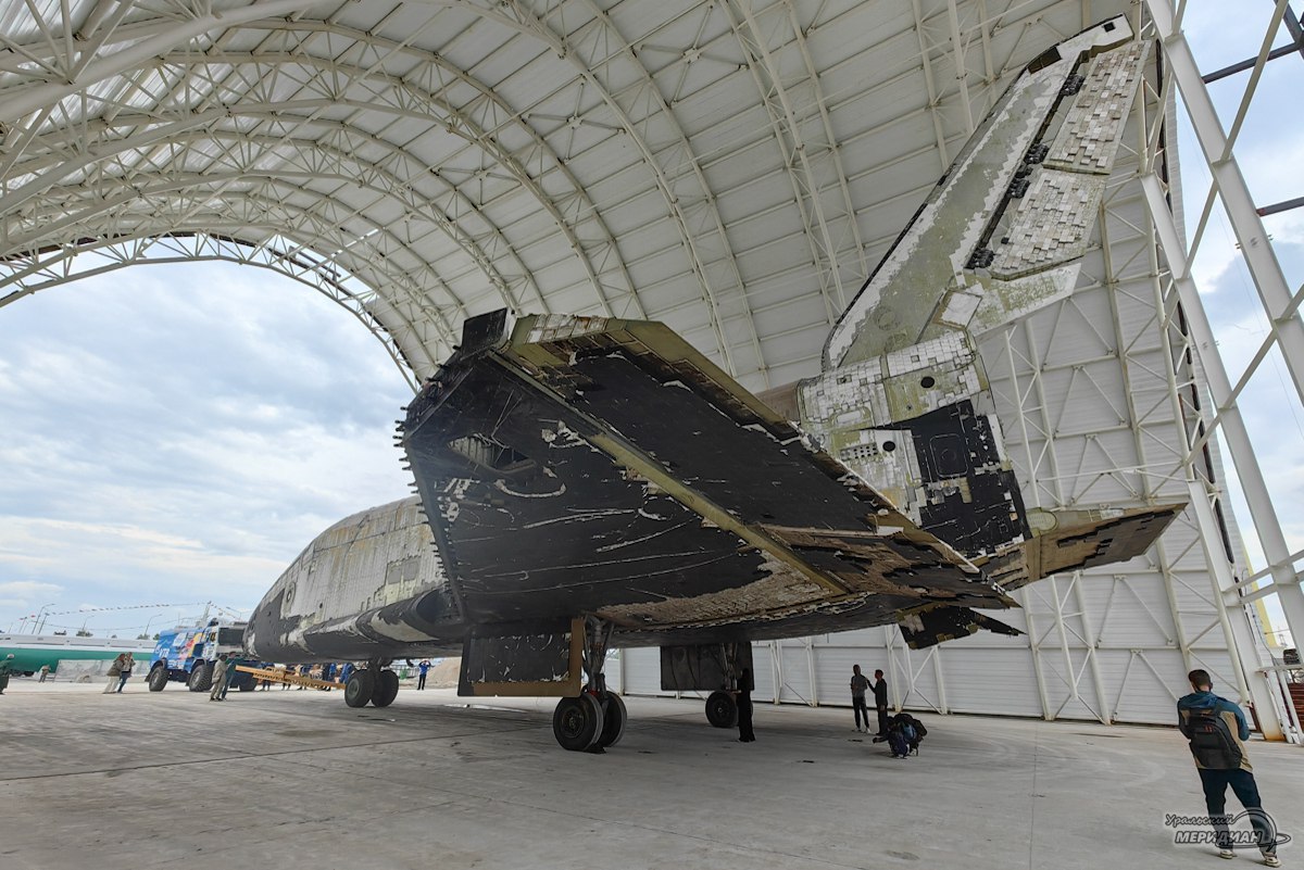 Космический корабль «Буран» закатили в ангар в Верхней Пышме В его транспортировке принимали участие пятикратный победитель «Ралли Дакар» Эдуард Николаев и заслуженный мастера спорта России Андрей Каргинов. Космический корабль «Буран» транспортировали при помощи другого уникального экспоната музея — автомобиля КАМАЗ-4326-9 VK, за рулем которого находился Каргинов. Масса «Бурана» фюзеляж и консоли крыльев — 56 т, в шесть раз больше грузовика КАМАЗ, но мощный профессионализм пилота позволили отбуксировать космический корабль в ангар за 3 минуты. Строительство павильона для орбитального космического корабля «Буран» в Верхней Пышме началось осенью прошлого года. На сегодняшний день почти завершены кровельные работы. Чтобы завершить строительство ангара космический корабль потребовалось доставить туда уже на этом этапе работ. «Уральский меридиан»