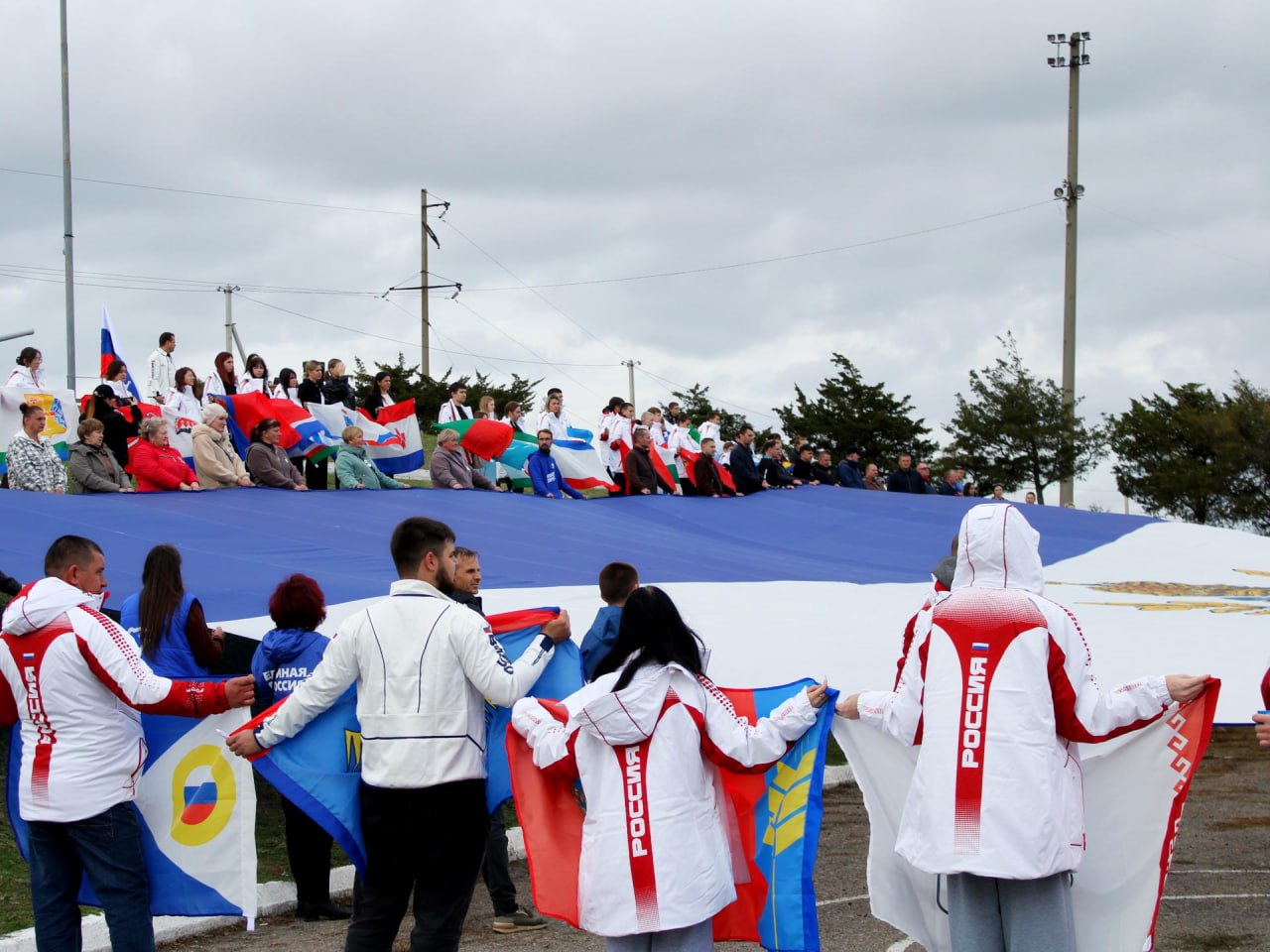 Спортсмены Херсонской области развернули 800 метровый флаг в преддверии Дня народного единства В преддверии Дня народного единства на площади у мемориала Защитникам Арабатской стрелки в селе Геническая Горка состоялось поистине историческое событие Выбор места проведения акции был глубоко символичным в Год 80 летия Великой Победы мы особенно остро осознаем ценность единства и преемственность поколений В рамках патриотической акции Энергия двух морей организованной Министерством спорта Херсонской области при поддержке партии Единая Россия спортсмены тренеры и жители региона развернули 37 метровое полотнище флага Херсонской области площадью 800 квадратных метров Огромный флаг Херсонской области развёрнутый на Генической Горке символ нашего единства силы и веры в общее будущее Сегодня на площади были и местные жители и гости из других регионов которые работают здесь помогают восстанавливать Херсонщину Каждый кто держал в руках флаг своего края республики всей России чувствовал что мы вместе заявил Губернатор Херсонской области Владимир Сальдо Под торжественные звуки гимна Российской Федерации гигантский флаг занял свое место в центре площади а знаменосцы со флагами всех 89 субъектов Российской Федерации образовали вокруг него живое кольцо единства В акции приняли участие более 500 человек представители спортивного сообщества волонтеры Молодой Гвардии Единой России местные жители и гости из других регионов страны На мероприятии присутствовали почетные гости Заместитель Председателя Правительства Херсонской области Сергей Черевко первый заместитель Председателя Херсонской областной Думы член фракции Единая Россия Елена Дмитрук первый заместитель руководителя фракции Единая Россия в региональном парламенте Александр Хлюстов Вместе с и о министра спорта Херсонской области Еленой Кирилловой они наградили спортсменов и работников спортивных школ за значительный вклад в развитие спорта на территории региона Как отметила Елена Кириллова Для каждого спортсмена возможность поднять флаг своей страны это особая честь и высшее признание заслуг Сегодня мы все стали частью большого патриотического движения которое укрепляет наше национальное единство Завершилось мероприятие торжественным возложением цветов к мемориалу Защитникам Арабатской стрелки в память о воинах павших за свободу и независимость нашей Родины Этот день еще раз доказал спорт объединяет людей воспитывает патриотов и служит фундаментом сильной единой России