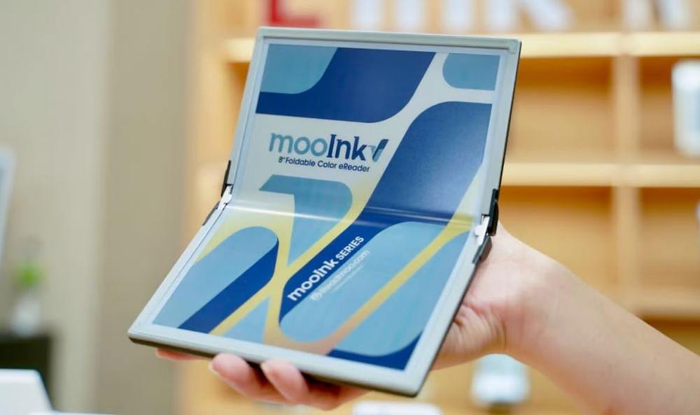 Первая в мире складная и полноцветная E Ink-книга в одном шаге от выпуска Компания Readmoo показала на выставке в Тайване полноцветную складную книгу-ридер на электронных черниалах. Новинка, получившая название mooInk V, сочетает в себе преимущества складных гаджетов, которые приобретают все большую популярность, и традиционного формата книги. «Читалка» оснащена цветным ePaper-дисплеем, разрешение которого составляет 300 пиксель/дюйм. При необходимости он складывается пополам, образуя 8-дюймовый экран. Такой формат позволяет читать цифровой контент, включая комиксы и иллюстрированные книги. Недостатком mooInk V является отсутствие штатной фронтальной подсветки, поэтому для чтения в условиях недостаточного освещения потребуется дополнительный источник света. В сложенном состоянии на месте сгиба появляется небольшой зазор, обусловленный толщиной слоя электронной бумаги. Тем не менее, панель ридера прошла тщательные испытания на прочность и выдерживает не менее 200 000 циклов открывания-закрывания. MooInk V весит около 255 г и готова к производству. Сведения о цене и дате старта продаж пока не озвучены.
