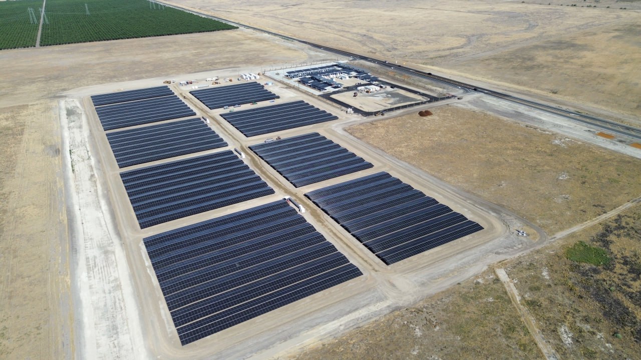 Компания Tesla открыла впечатляющую зарядную станцию на солнечных батареях в отдаленном районе Калифорнии. Эта инженерная инновация, получившая название Tesla Oasis, практически полностью получает энергию от солнечных лучей. Станция оборудована 168 зарядными стойками, из которых 84 уже введены в эксплуатацию. Энергетический комплекс включает 11 МВт солнечных батарей и 10 огромных аккумуляторов Tesla Megapack с общей емкостью 39 МВч. Процесс строительства занял всего 8 месяцев, что свидетельствует о невероятных темпах реализации такого амбициозного проекта. Располагается станция в городке Lost Hills, на маршруте Interstate 5, который связывает Лос-Анджелес и Сан-Франциско. Это стратегический выбор, так как данный маршрут является одним из самых загруженных для электромобилей в США. Характерной чертой станции является её уникальная схема работы. Местная электросеть может предоставить лишь 1.5 МВт мощности, что составляет менее 10 кВт на одну зарядную стойку.