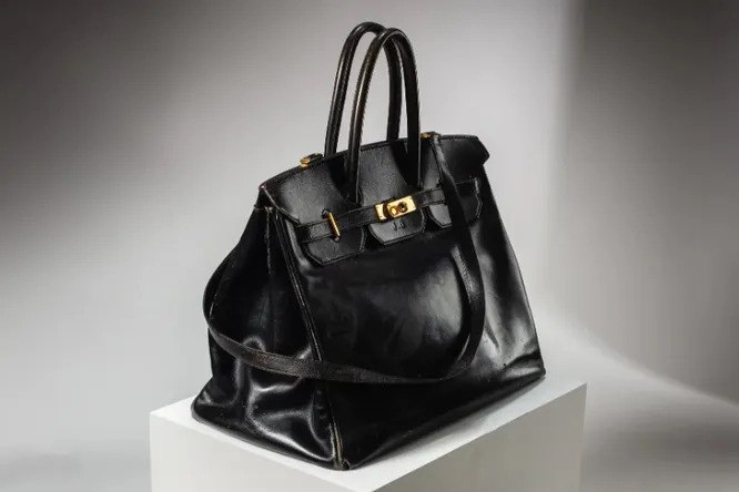 Сумку Джейн Биркин выставляют на аукцион. Этот аксессуар модный дом Hermes сделал по спецзаказу актрисы. Позже сумка стала прототипом самой дорогой и известной модели в мире. Торги организует дом Sotheby s, они начнутся в Париже 10 июля. Подробнее о сумке Birkin и ее первом экземпляре — в справке "Ъ FM": Сумка Birkin от французского модного дома Hermes — один из самых дорогих в мире аксессуаров. Их делают вручную и только во Франции. На одну сумку уходит около 18 часов, а в год Hermes выпускает лишь несколько экземпляров. Чтобы ее получить, покупатели занимают очередь и ждут от нескольких месяцев до пары лет. Первая сумка Birkin появилась в 1984 году: модель сделали по личному заказу Джейн Биркин. Это стало возможным после ее случайной встречи с директором Hermes в самолете. Тогда актриса пожаловалась, что ей не подходит ни одна сумочка Hermes из-за небольших размеров. Там же они набросали эскиз будущей модели Birkin. Первый экземпляр из черной кожи достался самой Джейн. Актриса носила сумку десять лет, пока в 1994-м не продала ее на аукционе. Деньги ушли благотворительной организации по борьбе со СПИДом. В 2000 году первая Birkin оказалась у частного коллекционера, известной как Кэтрин Би. При ней сумка выставлялась в музеях.