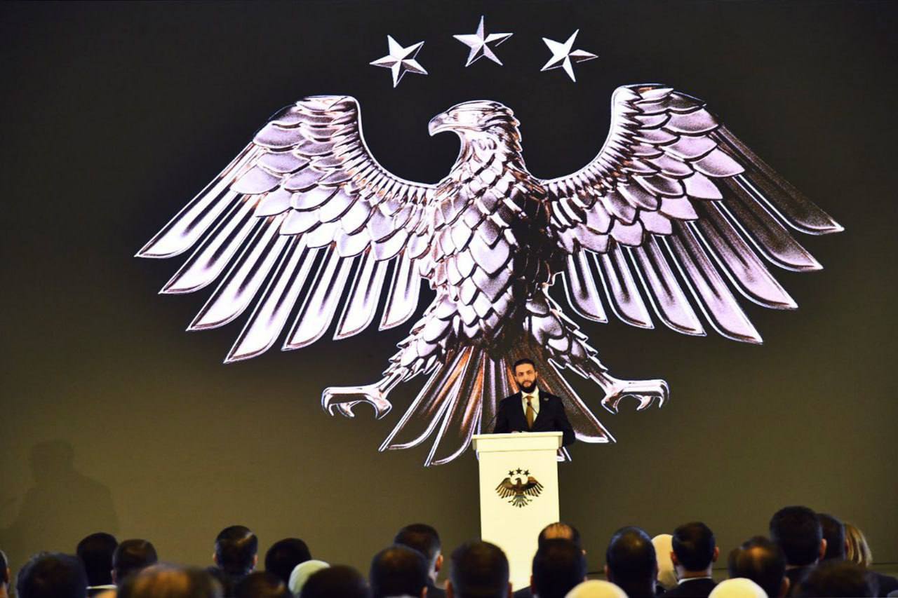 Президент Сирии объявил о начале “новой страницы” в истории страны По словам сирийского лидера, народ пережил худший период при прежнем режиме, но теперь Сирия начинает новый этап, в котором делается ставка на человеческий потенциал и национальное единство. Он подчеркнул, что новая визуальная идентичность страны символизирует стремление к развитию и “строительству человека”. На фото президент Сирии на фоне нового герба страны
