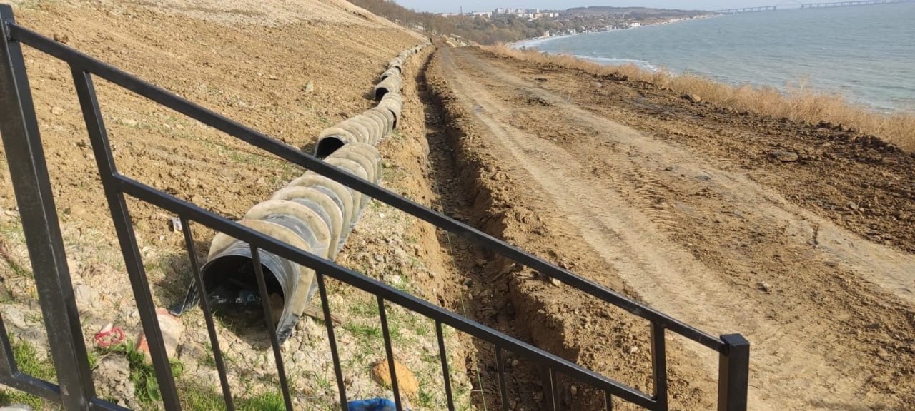 В Керчи завершается строительство противооползневых сооружений. На данный момент продолжается работа по планировке откосов — это важный элемент строительных и ландшафтных проектов. Данные мероприятия направлены на повышение устойчивости склонов, предотвращение эрозии и обеспечение безопасности объектов, расположенных в непосредственной близости от откосов. Кроме того, осуществляется монтаж водоотводных лотков. Эти конструкции предназначены для сбора и отвода поверхностных вод, что позволяет избежать накопления влаги и защитить строительные объекты, дорожное покрытие и садовые участки от эрозии и разрушений. Также проводятся работы по устройству покрытия Прибрежного спуска. Дорожное покрытие Прибрежного спуска, как и любое другое дорожное покрытие, должно гарантировать надежность, безопасность и долговечность в процессе эксплуатации.