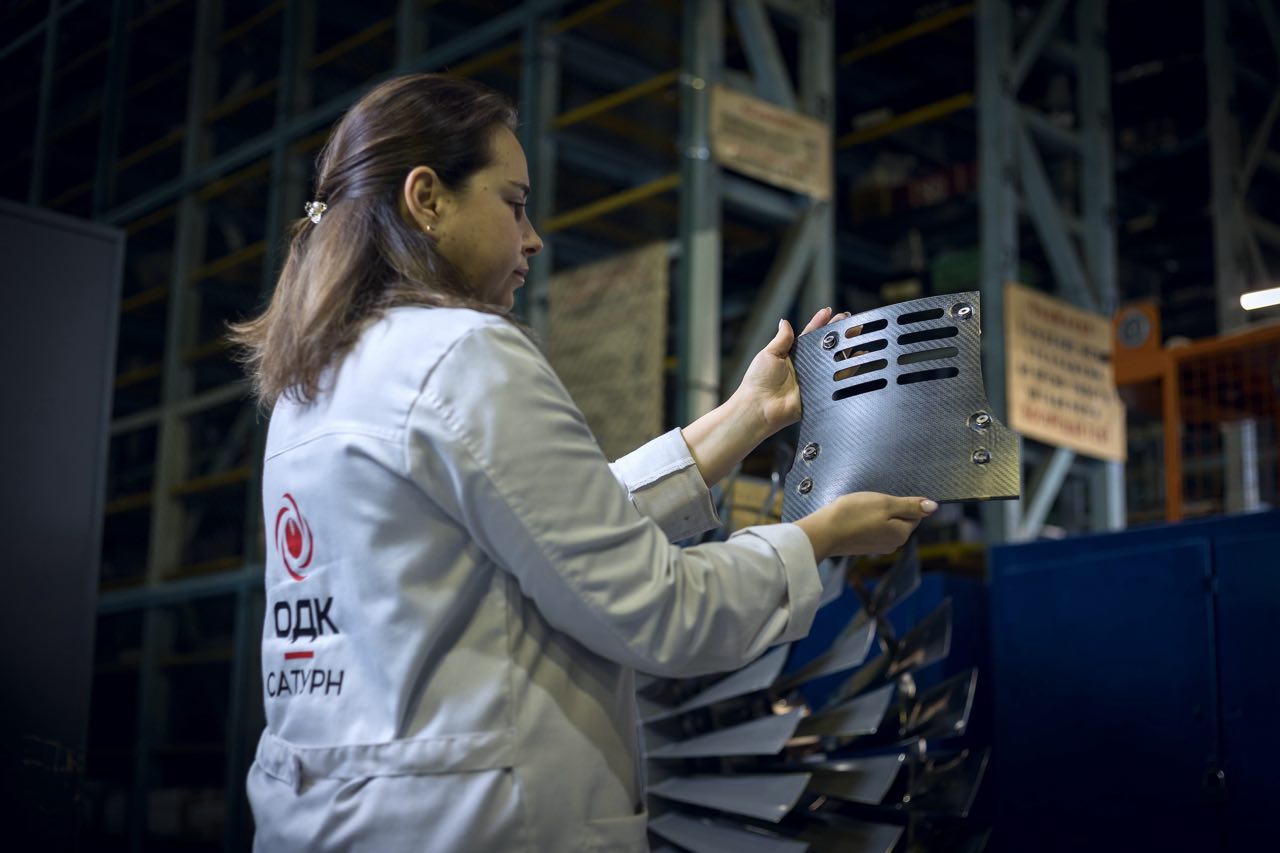 Специалисты предприятия ОДК Сатурн входящего в состав Объединённой двигателестроительной корпорации Госкорпорации Ростех разработали и внедрили принципиально новую российскую технологию переработки углепластика для изготовления внутренних панелей компрессора модернизированной версии авиадвигателя ПД 8 Использование лёгких и одновременно высокопрочных отечественных материалов позволит снизить массу двигателя повысить его топливную эффективность и уменьшить стоимость жизненного цикла Основой новой технологии стал российский углепластик ВКУ 65 разработанный в НИЦ Курчатовский институт ВИАМ на базе полиэфирэфиркетона и углеродной ткани Из него на ОДК Сатурн изготовлены опытные комплекты внутренних панелей компрессора для перспективной модификации ПД 8 В производстве применяется метод термоформования консолидированный материал нагревается в инфракрасной печи до температуры плавления связующего после чего прессуется до требуемой формы Такой способ даёт высокую точность равномерную толщину деталей и заметно ускоряет цикл производства Главный инженер ОДК Сатурн Игорь Ильин отметил что ВКУ 65 стал вторым российским материалом позволяющим изготавливать изделия из полимерных композиционных материалов методом термоформования По его словам это обеспечивает значительные преимущества по скорости и качеству изготовления На первом этапе предприятие изготовило два опытных комплекта внутренних панелей компрессора для следующей модификации ПД 8 и уже прорабатывает возможность аналогичным способом создавать верхний и нижний сектора двигателя ПД 14 Параллельно на предприятии внедрена новейшая лазерная установка серии СЛП520 для высокоточной резки деталей авиадвигателей Оборудование созданное по техническому заданию ОДК Сатурн на заводе в Зеленограде обеспечивает сложноконтурную резку прошивку мелкоразмерных отверстий и сварку элементов С момента введения в эксплуатацию в 2024 году трудоёмкость изготовления отверстий и пазов снизилась более чем на 70 а пропускная способность производства выросла без потери качества В результате реализации двух проектов предприятие смогло существенно сократить цикл изготовления ключевых деталей внедрить современные технологические решения и оборудование сопоставимые по точности и качеству с лучшими зарубежными аналогами За разработку и внедрение технологии переработки углепластика специалисты ОДК Сатурн и НИЦ Курчатовский институт ВИАМ были удостоены престижной премии Авиастроитель года в номинации За успехи в развитии диверсификации производства Среди лауреатов начальник отдела полимерных композиционных материалов ОДК Сатурн Николай Кулаков и ведущий специалист отдела Александр Почищалов Проект по внедрению новой лазерной установки также был отмечен дипломом конкурса в реализации участвовали главный инженер предприятия Игорь Ильин главный технолог Артур Берестевич а также специалисты инженерных подразделений Александр Орлов Светлана Пятунина и Илья Красавин ПД 8 новейший двухконтурный турбовентиляторный двигатель тягой восемь тонн созданный Объединённой двигателестроительной корпорацией Ростеха специально для ближнемагистральных самолётов Суперджет и самолёта амфибии Бе 200 Он разработан с применением современных российских материалов и технологий и является полностью отечественным изделием Работы по проекту стартовали в 2019 году В марте 2025 года начались сертификационные испытания ПД 8 в составе самолёта Суперджет 100 а в июне 2025 года полностью импортозамещённый Суперджет совершил первый длительный перелёт на двигателях ПД 8 В ходе сертификационных испытаний самолёт успешно прошёл тесты по защите двигателей от воды На ТАНТК имени Бериева уже ведётся подготовка к установке ПД 8 на самолёты амфибии Бе 200 Альтаир Комплексная работа предприятий Ростеха демонстрирует способность России создавать собственные высокотехнологичные решения в авиадвигателестроении обеспечивая устойчивое развитие отрасли и независимость от зарубежных поставщиков Читай в Max Читай в Telegram Смотри на RUTUBE