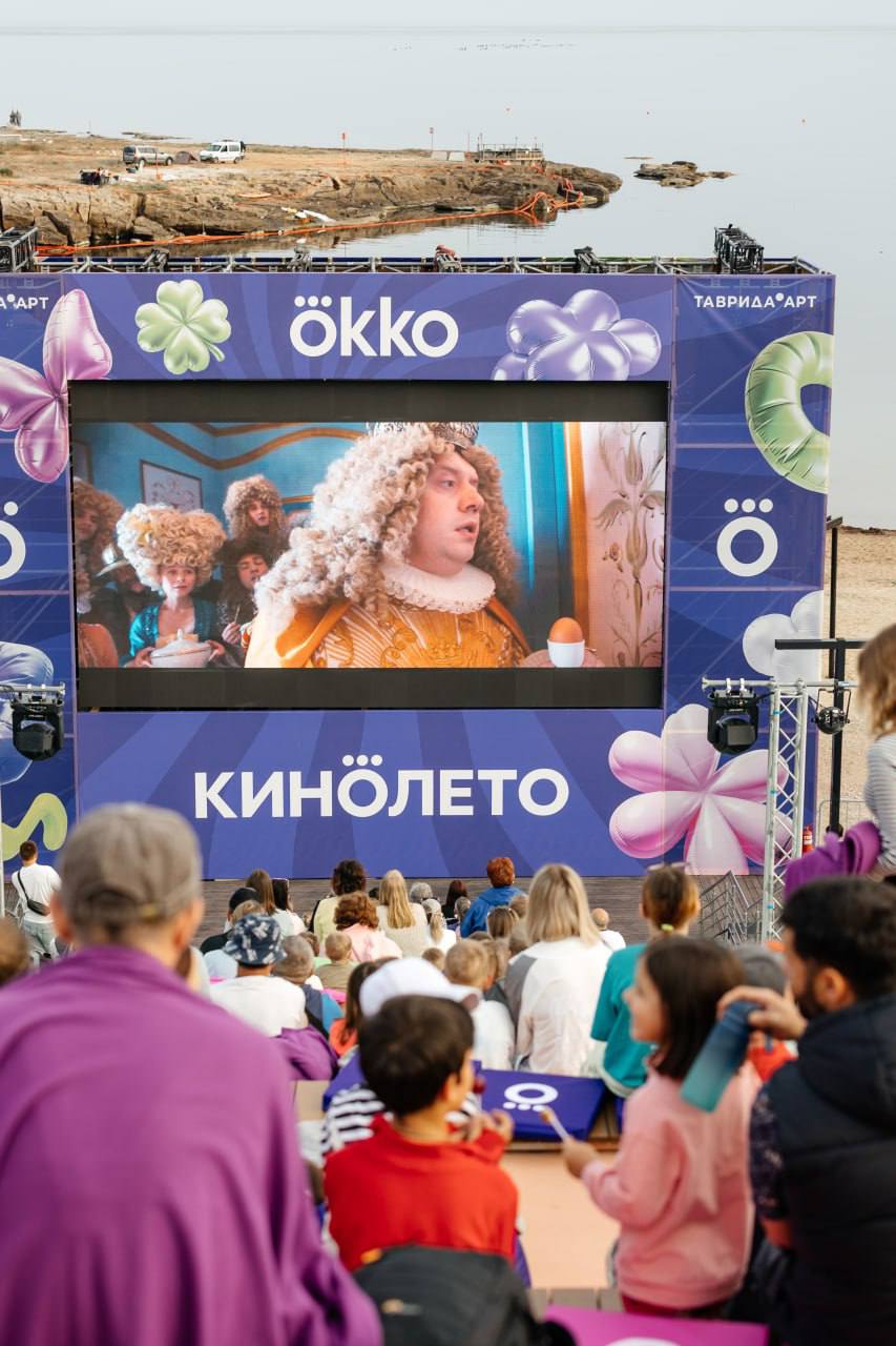 Под Судаком этим летом показывают кино под открытым небом! На территории Академии «Меганом» в День защиты детей начал работу летний кинотеатр Okko. Показы уже проходят, в День защиты детей посвящены семейным фильмам и фильмам-победителям кинофестиваля «Мост». Кинотеатр работает каждую пятницу, субботу и воскресенье — по 2 сеанса в день, а с 1 по 3 августа, во время фестиваля «Таврида.АРТ», — будут показывать по 3 сеанса Найти кинотеатр можно на лестнице рядом с пляжем «Академический» — открытый воздух, вид на море, удобные скамейки и большой экран. Вход свободный, регистрация не требуется. Расписание летнего кинотеатра будет в телеграм-канале Города молодых творцов