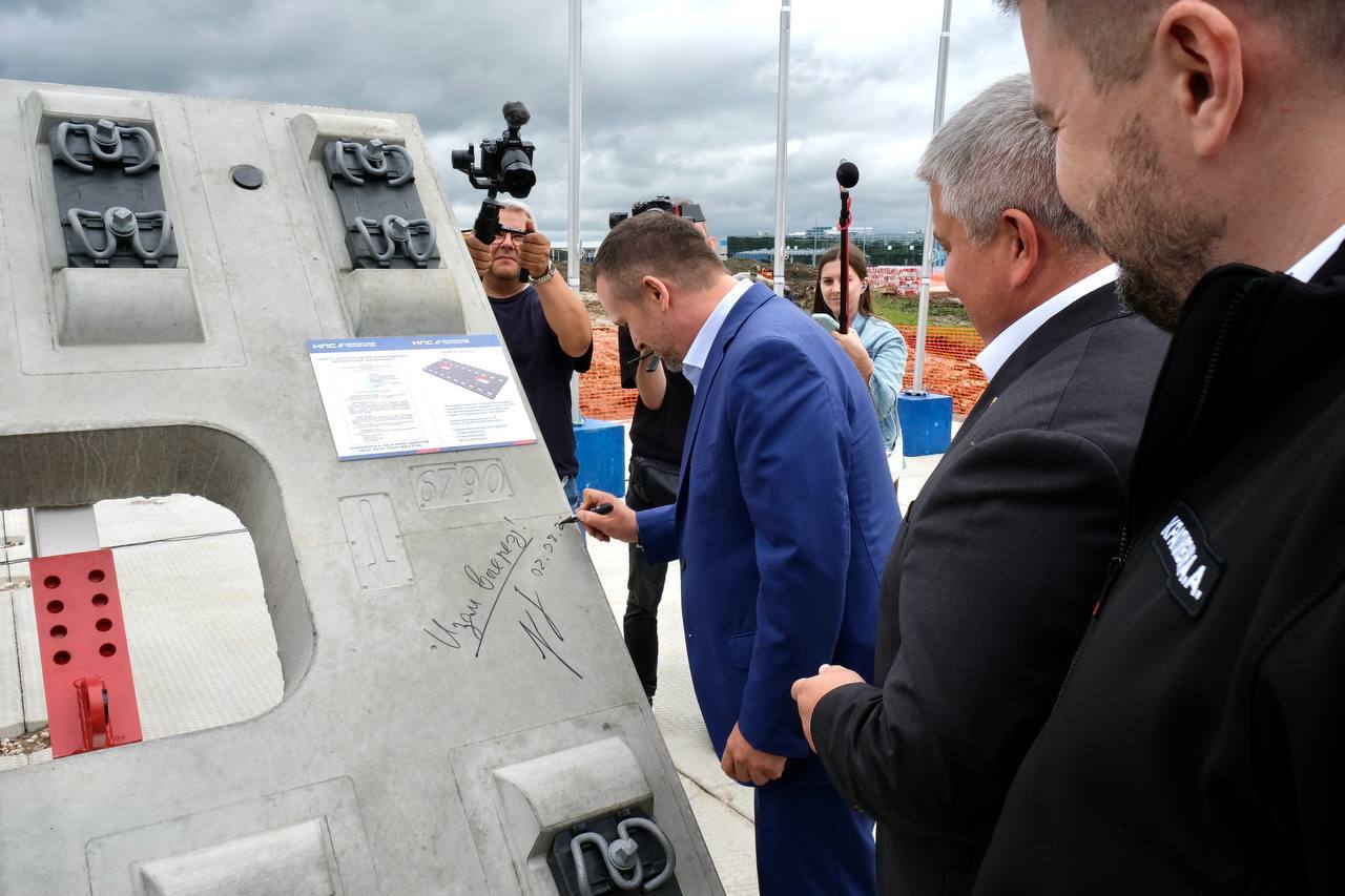 В Великом Новгороде Нацпроектстрой развернул строительство первого в стране роботизированного завода ЖБИ для высокоскоростных магистралей. Общий объем инвестиций в проект оценивается в 12 миллиардов рублей.  Сегодня на месте будущего завода установили закладной камень. Церемония прошла при участии министра транспорта РФ Андрея Никитина, врио губернатора Новгородской области Александра Дронова и генерального директора ГК Нацпроектстрой Алексея Крапивина.  «Сегодняшнее событие – важная веха в реализации одного из ключевых инфраструктурных проектов страны. ВСМ – это проект, который меняет представление о транспортной системе России. Мы говорим о новой скорости, новой связности и новой экономике регионов. Уже на первом этапе создается транспортный каркас, который не только объединит крупнейшие города, но и сформирует базу для долгосрочного роста и технологического развития», – заявил Андрей Никитин.  «Мы получаем не просто новый завод, а целый технологический кластер, который принесет новые возможности для развития смежных отраслей. Наш регион войдет в принципиально новую транспортную реальность – из Великого Новгорода до Москвы или Санкт-Петербурга можно будет добраться за рекордно короткое время. Это кардинально изменит инвестиционную привлекательность области и качество жизни новгородцев», – подчеркнул Александр Дронов.  «Чтобы обеспечить материалами ВСМ-1, мы в сжатые сроки создаем одно из крупнейших в стране ЖБИ-предприятий. От топосъемки территории до вывода завода на полную мощность пройдет чуть больше года. Уже в апреле 2026 года мы планируем приступить к пусконаладке производственной линии и выпустить пилотную партию плит, а в третьем квартале 2026 – наладить серийный выпуск продукции», – рассказал Алексей Крапивин, генеральный директор Нацпроектстроя.  Предприятие закроет до двух третей годовой потребности в плитах для эстакад и земляного полотна ВСМ-1 Москва – Санкт-Петербург. Здесь будут выпускать железобетонные плиты, необходимые для безбалластного пути ВСМ, а также полимерный упругий слой для защиты конструкции от повреждений.  Мощность завода – более 100 тысяч сборочных единиц и более 3,6 миллиона квадратных метров полимерных материалов в год.  #НПС_новости #ВСМ1