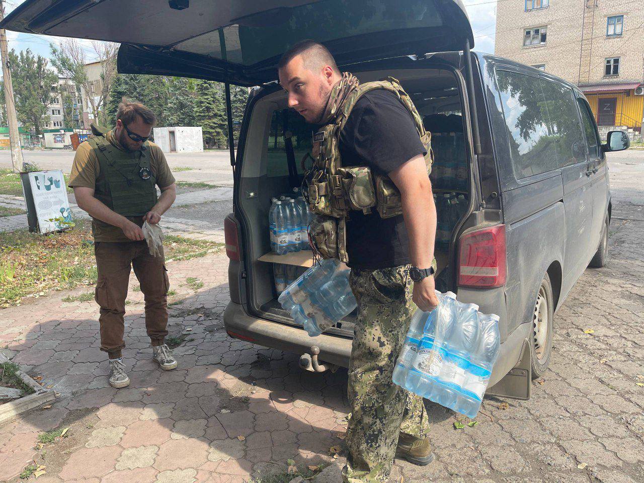 Ситуация с водой в Горнякской агломерации.   Из увиденного нами пока что самая острая пробема с водой — в горнякской агломерации. Это город Горняк и окрестные сёла: Желанное, Зорино, Новоселидово, Кураховка. Горняк находится совсем близко к линии фронта — всего 15-20 километров до противника.  Здесь вся власть под контролем военно-гражданской администрации  ВГА , которая отвечает за всё — от медицины до МЧС. В условиях постоянных атак и ограниченных ресурсов приходится восстанавливать разрушенный город их силами. Вдобавок ко всему сюда ещё долетают вражеские дроны, а подвоз топлива — настоящая дорога войны с воронками и сгоревшими машинами на обочинах. Для этих поездок мы всегда берём с собой бронежилеты и дрон-детекторы.  Сейчас в агломерации живёт больше 1500 человек. Но воды здесь нет. Местные говорят, что насосная станция перестала справляться.   Причин несколько:  1. Из-за засухи вода уходит из скважин.  2. Насосы перегорают на жаре и выходят из строя, а для их работы нужно топливо, которого тоже не хватает.  Оставшаяся вода перенасыщена минералами и щелочью, пить её вредно, но другого источника нет.  Это приводит к обострениям заболеваний у пожилых людей — камни в почках, скачки давления даже у молодых.  В прошлых миссиях мы привозили в Горняк медикаменты, а в июне — мотоцикл для главного медика города, чтобы он мог развозить лекарства по окрестным сёлам и помогать раненым. Мотоцикл отлично справляется, а начальник медицинской службы — тем более   Мы привезли почти 4000 литров воды. И вскоре доставим ещё столько же.   Конечно, это капля в море, но для местных жителей это огромная помощь, особенно в такой тяжёлый период.   К тому же большая фура слишком заметна, чтобы ехать по обстреливаемой дороге. Поэтому воду мы доставляем менее заметными автомобилями.  Поддержать можно — здесь.