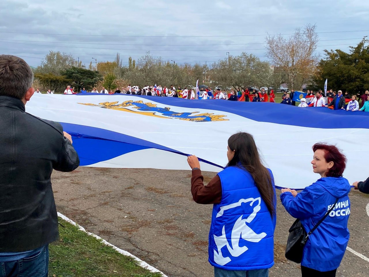 Спортсмены Херсонской области развернули 800 метровый флаг в преддверии Дня народного единства В преддверии Дня народного единства на площади у мемориала Защитникам Арабатской стрелки в селе Геническая Горка состоялось поистине историческое событие Выбор места проведения акции был глубоко символичным в Год 80 летия Великой Победы мы особенно остро осознаем ценность единства и преемственность поколений В рамках патриотической акции Энергия двух морей организованной Министерством спорта Херсонской области при поддержке партии Единая Россия спортсмены тренеры и жители региона развернули 37 метровое полотнище флага Херсонской области площадью 800 квадратных метров Огромный флаг Херсонской области развёрнутый на Генической Горке символ нашего единства силы и веры в общее будущее Сегодня на площади были и местные жители и гости из других регионов которые работают здесь помогают восстанавливать Херсонщину Каждый кто держал в руках флаг своего края республики всей России чувствовал что мы вместе заявил Губернатор Херсонской области Владимир Сальдо Под торжественные звуки гимна Российской Федерации гигантский флаг занял свое место в центре площади а знаменосцы со флагами всех 89 субъектов Российской Федерации образовали вокруг него живое кольцо единства В акции приняли участие более 500 человек представители спортивного сообщества волонтеры Молодой Гвардии Единой России местные жители и гости из других регионов страны На мероприятии присутствовали почетные гости Заместитель Председателя Правительства Херсонской области Сергей Черевко первый заместитель Председателя Херсонской областной Думы член фракции Единая Россия Елена Дмитрук первый заместитель руководителя фракции Единая Россия в региональном парламенте Александр Хлюстов Вместе с и о министра спорта Херсонской области Еленой Кирилловой они наградили спортсменов и работников спортивных школ за значительный вклад в развитие спорта на территории региона Как отметила Елена Кириллова Для каждого спортсмена возможность поднять флаг своей страны это особая честь и высшее признание заслуг Сегодня мы все стали частью большого патриотического движения которое укрепляет наше национальное единство Завершилось мероприятие торжественным возложением цветов к мемориалу Защитникам Арабатской стрелки в память о воинах павших за свободу и независимость нашей Родины