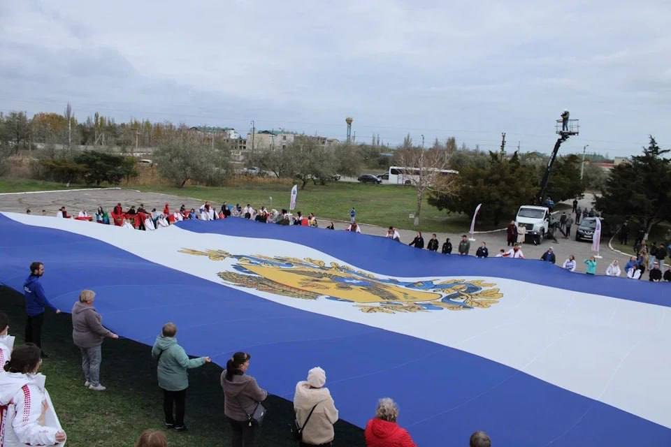 В преддверии Дня народного единства в селе Геническая Горка Херсонской области развернули флаг площадью 800 квадратных метров Акцию провели у мемориала защитникам Арабатской стрелки В ней приняли участие более 500 человек члены Единой России волонтёры молодёжь и юные спортсмены На мероприятии представили флаги всех 89 субъектов России в знак единения со страной В финале гости возложили цветы к мемориалу в память о воинах погибших за свободу и независимость страны