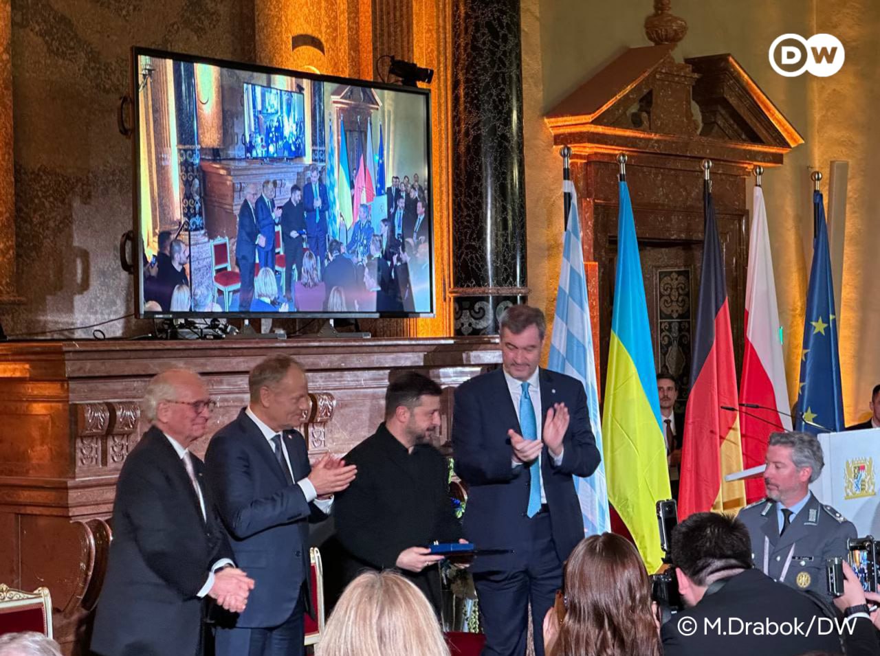 Зеленский принял премию за мужество для украинского народа Украинский народ награжден премией имени Эвальда фон Клейста которую организаторы Мюнхенской конференции по безопасности MSC ежегодно вручают за вклад в международное сотрудничество и разрешение конфликтов Премия была присуждена украинцам за мужество и готовность оказывать сопротивление агрессору На вручении премии Зеленский поблагодарил всех партнеров Украины которые помогают стране защищаться от вторжения РФ Люди в зале встали приветствовав президента Украины овациями передает корреспондент DW Среди лауреатов премии фон Клейста прошлых лет генеральный секретарь НАТО Йенс Столтенберг бывший канцлер Германии Ангела Меркель ООН и Организация по безопасности и сотрудничеству в Европе ОБСЕ dwglavnoe