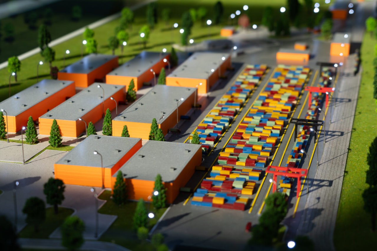 В Ташкентской области стартовало строительство логистического центра Silkway 15 ноября 2025 года в Ташкентской области официально началось строительство первой очереди многопрофильного логистического центра Silkway Central Asia Торжественный запуск проекта прошёл в формате узбекско казахстанского телемоста с участием Президента Казахстана Касым Жомарта Токаева и Президента Узбекистана Шавката Мирзиёева Проект реализуется совместным предприятием SILKWAY Central Asia созданным PTC Holding и АО Узбекистон темир йуллари Новый центр разместится на территории площадью 159 4 га в Янгиюльском районе и станет ключевым элементом инфраструктуры Срединного коридора обеспечивая значительные возможности для международной логистики и транзита грузов Первая очередь строительства предполагает создание современной контейнерной складской и терминальной инфраструктуры В рамках проекта планируется строительство 28 4 км железнодорожных путей соединяющих хаб с Казахстаном Ферганской долиной и Самаркандским направлением Общая площадь контейнерных площадок составит 172 тыс кв м склады класса А и В 167 тыс кв м включая холодильные и химические помещения Предусмотрены индустриально промышленная зона торгово выставочный центр площадью до 18 7 тыс кв м автомобильный мост для доступа на территорию и будущий железнодорожный путепровод а также переустройство высоковольтных линий электропередачи и подземных водоводов Пропускная способность центра к 2035 году прогнозируется на уровне до 3 млн тонн грузов в год Акционер PTC Holding Данияр Абулгазин отметил что переход проекта в строительную фазу является важным этапом позволяющим реализовать совместную инфраструктурную стратегию Казахстана и Узбекистана опираясь на ранее достигнутые соглашения Строительные работы ведутся в соответствии с утверждённым графиком продолжается возведение автомобильного моста через канал Джун формируется подъездная дорога к будущему терминалу завершается монтаж периметрального ограждения После ввода объекта в эксплуатацию на хабе будет создано около 700 рабочих мест что усилит социально экономический эффект проекта и расширит возможности для бизнеса в Янгиюльском районе Данияр Абулгазин подчеркнул что проект будет способствовать устойчивому развитию территории и формированию долгосрочных возможностей для профессиональной занятости и предпринимательства Запуск строительства стал продолжением договорённостей достигнутых президентами Казахстана и Узбекистана в декабре 2022 года закреплённых в межправительственных документах В последующие годы были выполнены проектные инженерные и организационные работы позволившие перейти к практической реализации масштабного логистического центра Telegram Facebook Instagram LinkedIn