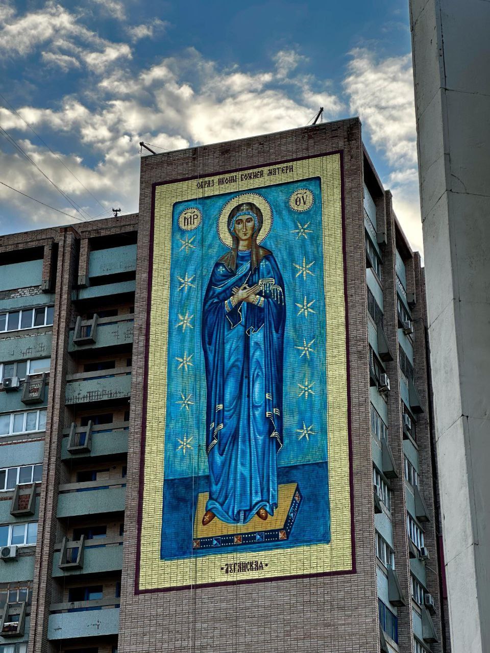 В Луганске появился уникальный мурал, посвященный Богородице Луганской На высоте 50 метров, откуда открывается потрясающая панорама города — видны Камброд, центральные улицы и восточные кварталы, — теперь красуется величественное изображение Богородицы Луганской. Мурал станет не только украшением города, но и символом духовности и единства для жителей региона. Над проектом работает команда талантливых художников-монументалистов из Краснодара, Самарской области и Москвы. Их опыт и мастерство позволили воплотить в жизнь масштабную задумку, которая уже привлекает внимание горожан и гостей Луганска. Проект получил благословение митрополита Луганского и Алчевского Пантелеимона. Инициатором создания мурала стал настоятель храма Александра Невского архимандрит Макарий Любавцев. Сейчас работа находится на завершающем этапе — осталось нанести защитный лак, который сохранит изображение на долгие годы. Мурал с образом Богородицы Луганской — это символ веры, надежды и любви к родному краю. Он станет местом притяжения для всех, кто ценит духовные и культурные ценности. Фото: Луганскинформцентр