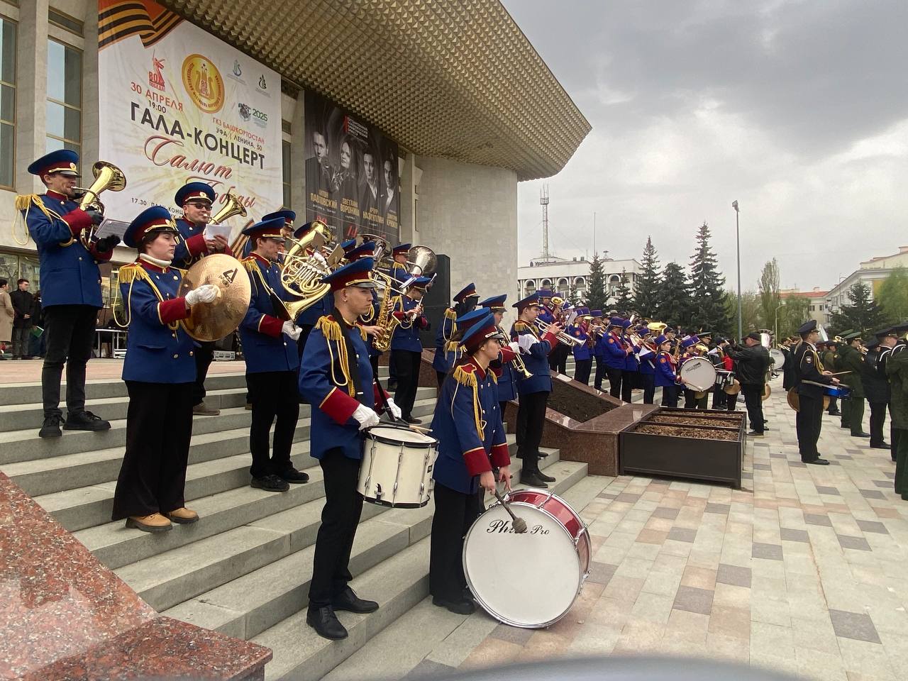 В Уфе на площади перед ГКЗ «Башкортостан» идет в эти минуты концерт духовых оркестров «Салют Победы». В программе военные марши и песни. Зрители подпевают.