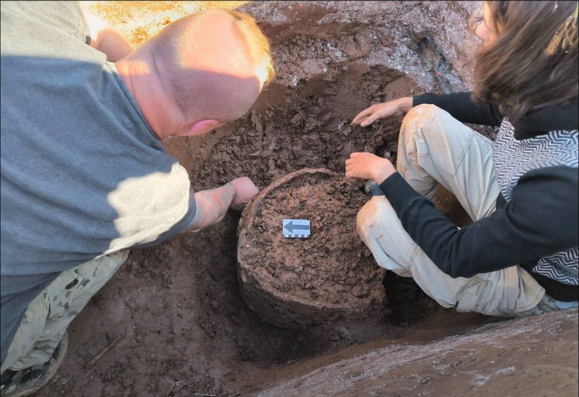 Горшок возрастом 6 000 лет. Новгородские археологи обнаружили удивительный предмет  Отряд Центра археологических исследований Новгородского университета во время разведки на берегу Волхова обнаружил керамический горшок. Предварительно, предмет был задействован в хозяйстве в IV тысячелетии до нашей эры.  Горшок столь почтенного возраста оказался целым, его диаметр 60 см.  «Уникальность находки состоит в том, что она — из культурного слоя, имеет научный контекст, обнаружена в ходе исследовательских работ и при этом представляет собою целую форму», — пояснила руководитель отряда Центра археологических исследований Екатерина Борисевич.  На Северо-Западе России такие находки единичны.  Горшок обнаружился в центре заложенного шурфа, и это тоже удивительно — шурф гораздо меньше раскопа. Находка пряталась в глине, открывшейся под толстым слоем ракушек. Сняв глиняные комки с внешней стороны, археологи увидели орнамент.  Как считают в университетском Центре археологических исследований, горшок можно отнести к культуре гребенчато-ямочной керамики. Это поздний неолит.  Почему сосуд оказался запечатанным в глине прямо на берегу реки, пока остается загадкой. Возможно, внезапно поднялась вода, предполагают археологи: место раскопа и сейчас — зона затопления.  Фото: Старорусская археологическая экспедиция НовГУ