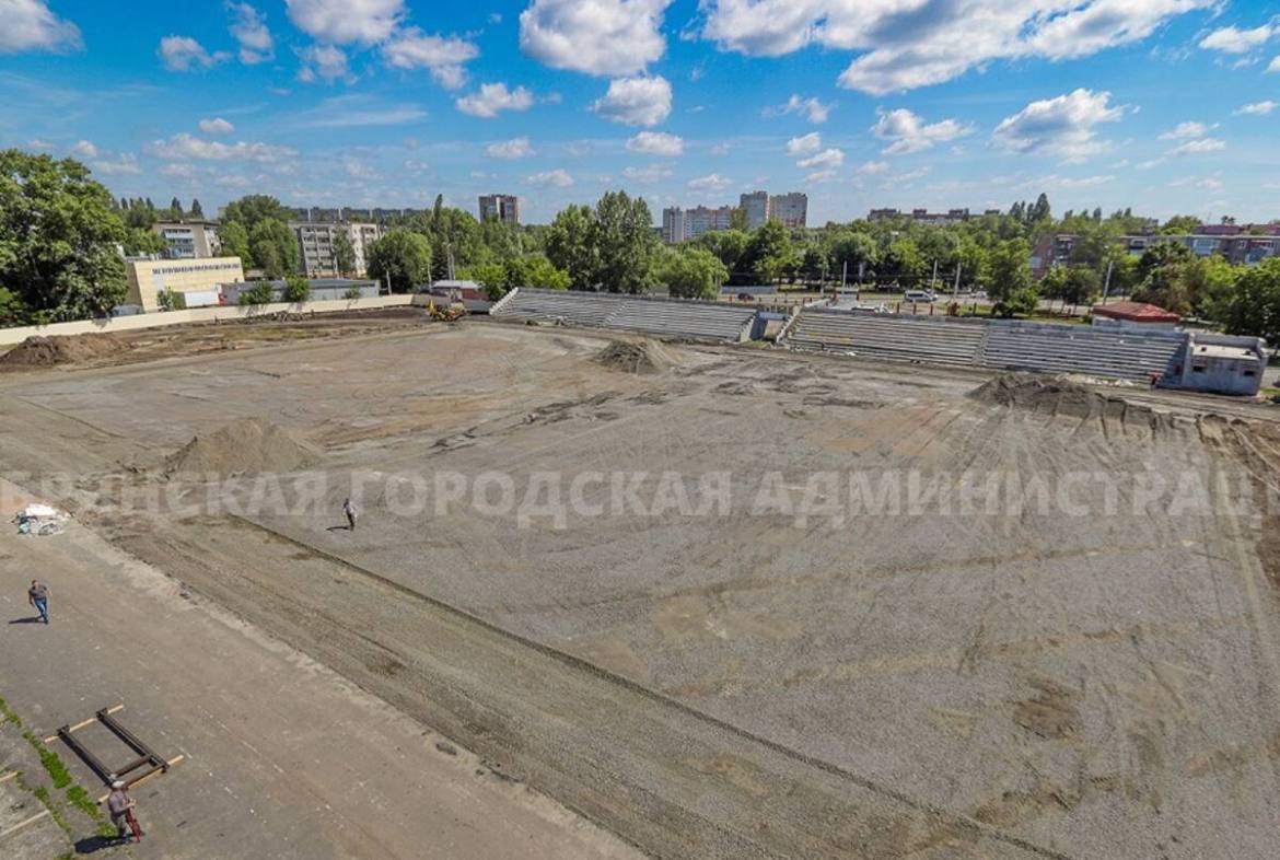 В Володарском районе полным ходом идет капремонт стадиона Брянских партизан Строители демонтировали старый газон и элементы подтрибунных помещений, отправив их на утилизацию. Подготовлена новая дренажная система с насосной станцией для отвода воды. На объект завезено 13 вагонов щебня — основа для будущего стадиона. Вскоре начнется укладка геотекстиля, искусственной травы, кварцевого песка и резиновой крошки. Подрядчик работает с опережением графика, как поручил мэр Александр Макаров. Завершается чистовая отделка трибун, где установят 1 200 кресел, что вдвое увеличит вместимость. Также вокруг поля появятся 4 беговые дорожки. Ежедневно на объекте трудятся до 40 человек с использованием тяжелой техники. Стоимость проекта превышает 116 млн рублей. Брянский навигатор