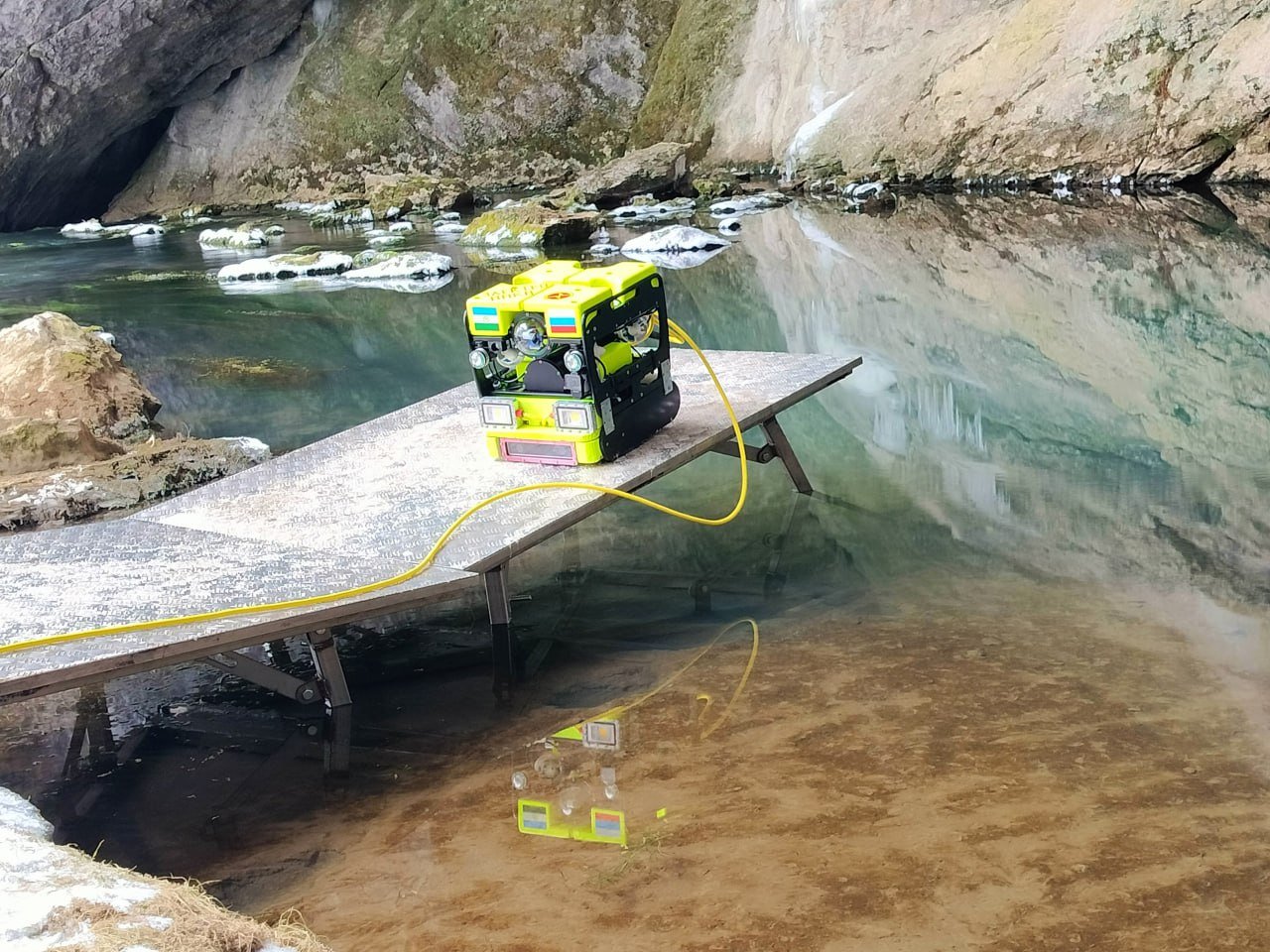 В Башкирии дрон погрузили в воды озера пещеры Шульган-Таш  В Башкирии началось исследование Голубого озера в пещере Шульган-Таш с помощью подводного дрона. Экспедиция в Бурзянском районе включает изучение подводных участков и сифонов, ранее недоступных для исследования. Озеро, образованное рекой Шульган, представляет собой источник воклюзного типа.  В первый день дрон преодолел 36 метров по каменному тоннелю и успешно вернулся. Тестовое погружение выявило сложные участки маршрута с резкими поворотами и выступами. Аппарат подключен к генераторам через 200-метровый кабель, что обеспечивает его длительное пребывание под водой.  Разработчик дрона, уфимский инженер Ярослав Литвинов, потратил восемь месяцев на создание надежного устройства. В экспедиции также участвует лучший водолаз России Александр Хижняк, который помогает оператору управлять дроном в сложных условиях. Он подчеркнул важность современных технологий для безопасности исследований, особенно после трагедии 2019 года, когда погиб водолаз.  Директор музея-заповедника Фавзил Маликов отметил, что исследование подводной части будет продолжаться несколько лет с целью создания единой карты Шульган-Таша. Благодаря таким энтузиастам, как Литвинов, и современным технологиям, работа будет проводиться с минимальным риском для жизни исследователей.    Обратная связь   Подписаться