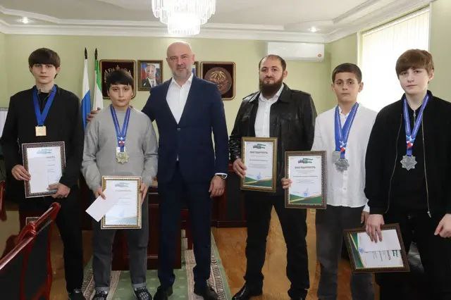 В Назрани чествовали победителей и призеров мирового первенства по шахбоксу В администрации города Назрань приветствовали юных представителей республики продемонстрировавших впечатляющие достижения на международной арене в шахбоксе сравнительно новом виде спорта На чемпионате мира прошедшем в сентябре в Сербии российская сборная завоевала лидирующую позицию в общекомандном зачете и спортсмены из Ингушетии внесли существенный вклад в этот успех По информации предоставленной газете Ингушетия представителями муниципалитета Илез Баркинхоев стал чемпионом мира в то время как Мухаммад Бопхоев и Умар Цуроев удостоились серебряных медалей Кроме того Осман Баркинхоев завоевал серебро в этой же дисциплине на Всемирных играх проходивших в Чувашии Шахбокс представляет собой уникальный синтез шахмат и бокса в котором участники соревнуются как в интеллектуальной игре так и в поединке Соревновательный процесс состоит из 11 раундов продолжительностью три минуты каждый в которых шахматная игра чередуется с боксерскими поединками Победа может быть достигнута либо нокаутом на ринге либо объявлением мата на шахматной доске Президент Федерации шахбокса Ингушетии Ваха Баркинхоев и тренер Ахмед Аушев отмечают стремительный рост популярности этого вида спорта в России Он объединяет в себе шахматы и бокс требуя от спортсменов не только физической силы и выносливости но и стратегического мышления концентрации и быстроты принятия решений как на ринге так и за шахматной доской Мэр города Руслан Оздоев поздравил молодых атлетов и их наставников с заслуженными наградами У нас очень талантливое поколение энергичное целеустремленное и многообещающее Я уверен что мы еще не раз услышим о победах ингушских спортсменов в том числе и в дисциплине шахбокс Поистине уникальный вид спорта и вы большие молодцы что демонстрируете такие впечатляющие результаты сразу в двух областях ПОДПИСАТЬСЯ ПРЕДЛОЖИТЬ НОВОСТЬ